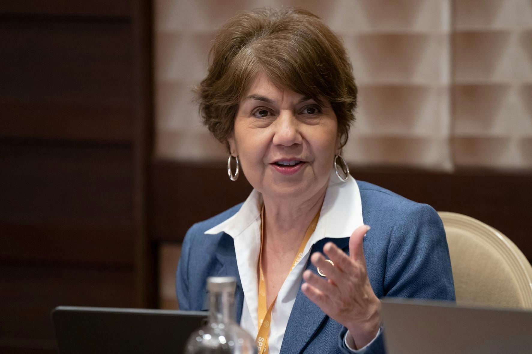 A woman in a blue blazer gestures while speaking during a meeting.