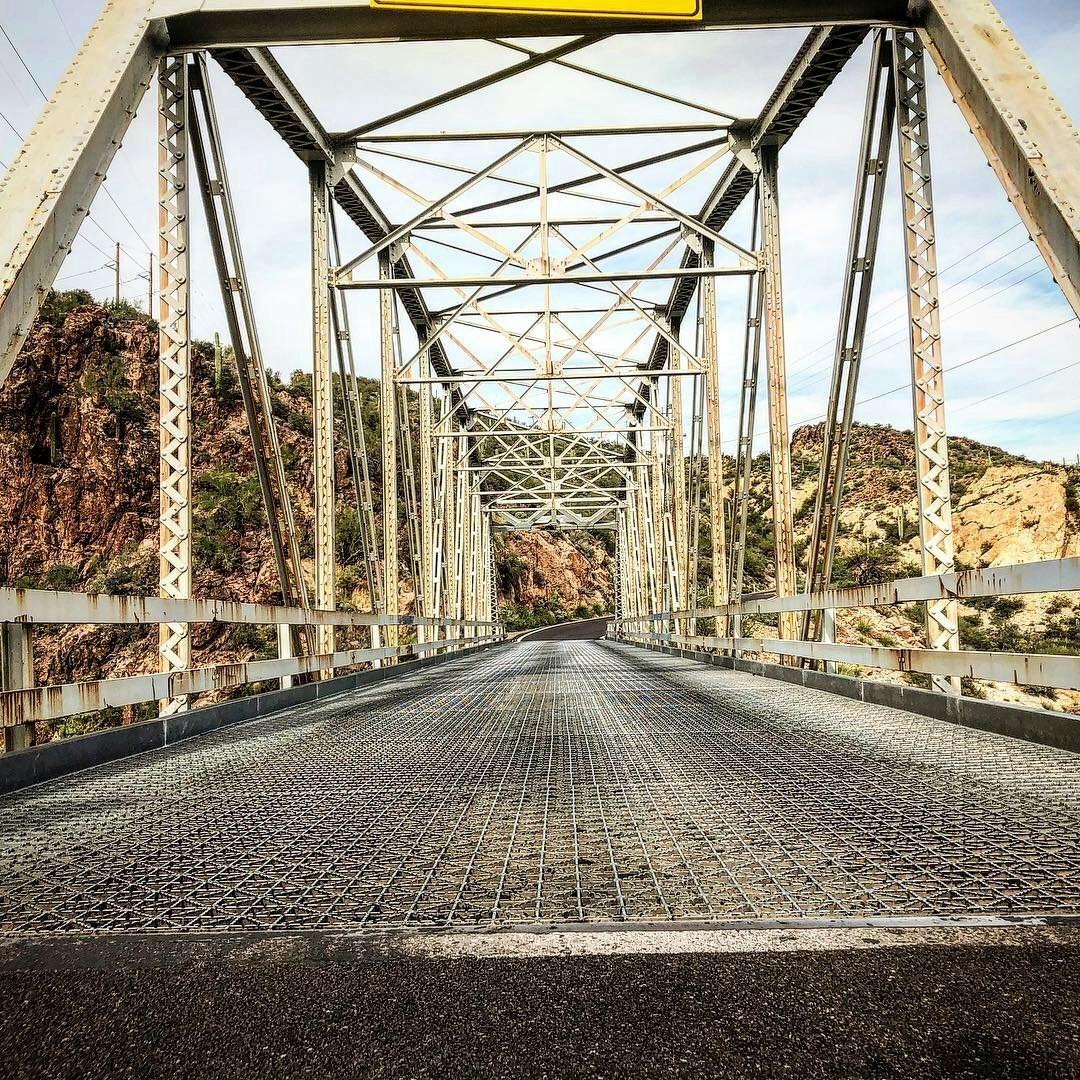 A metal truss bridge over a rocky landscape, with a grid-like road surface.
