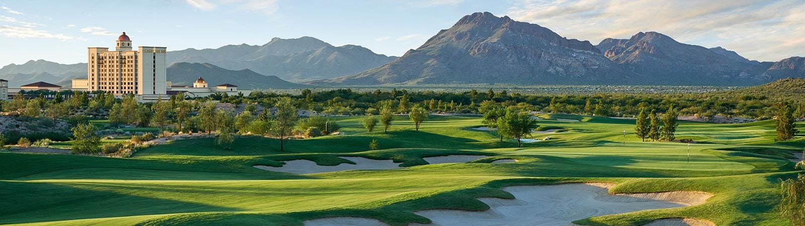 A green golf course with sand traps, mountains in the background, and a large building with a dome.