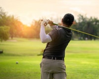 Golfer swings on a lush course at sunset.