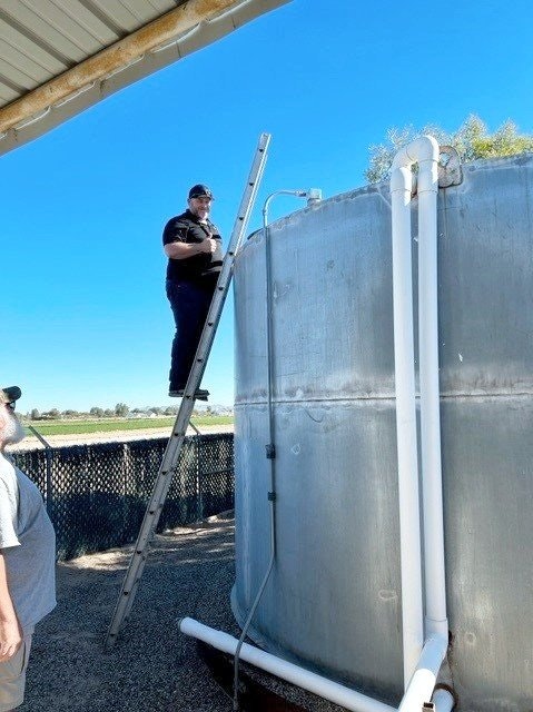 A person stands on a ladder inspecting a large metal tank outdoors.