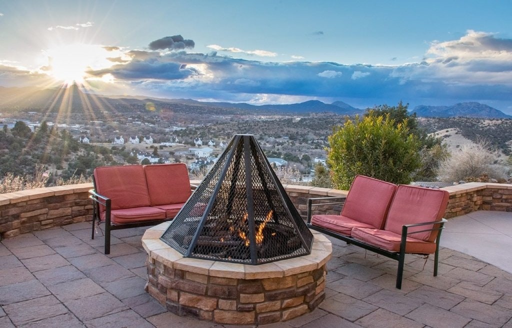 Outdoor seating area with red chairs around a fire pit on a stone patio, overlooking a scenic landscape at sunset.