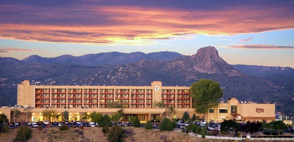 A large hotel building with a parking lot, set against a mountainous landscape at sunset.