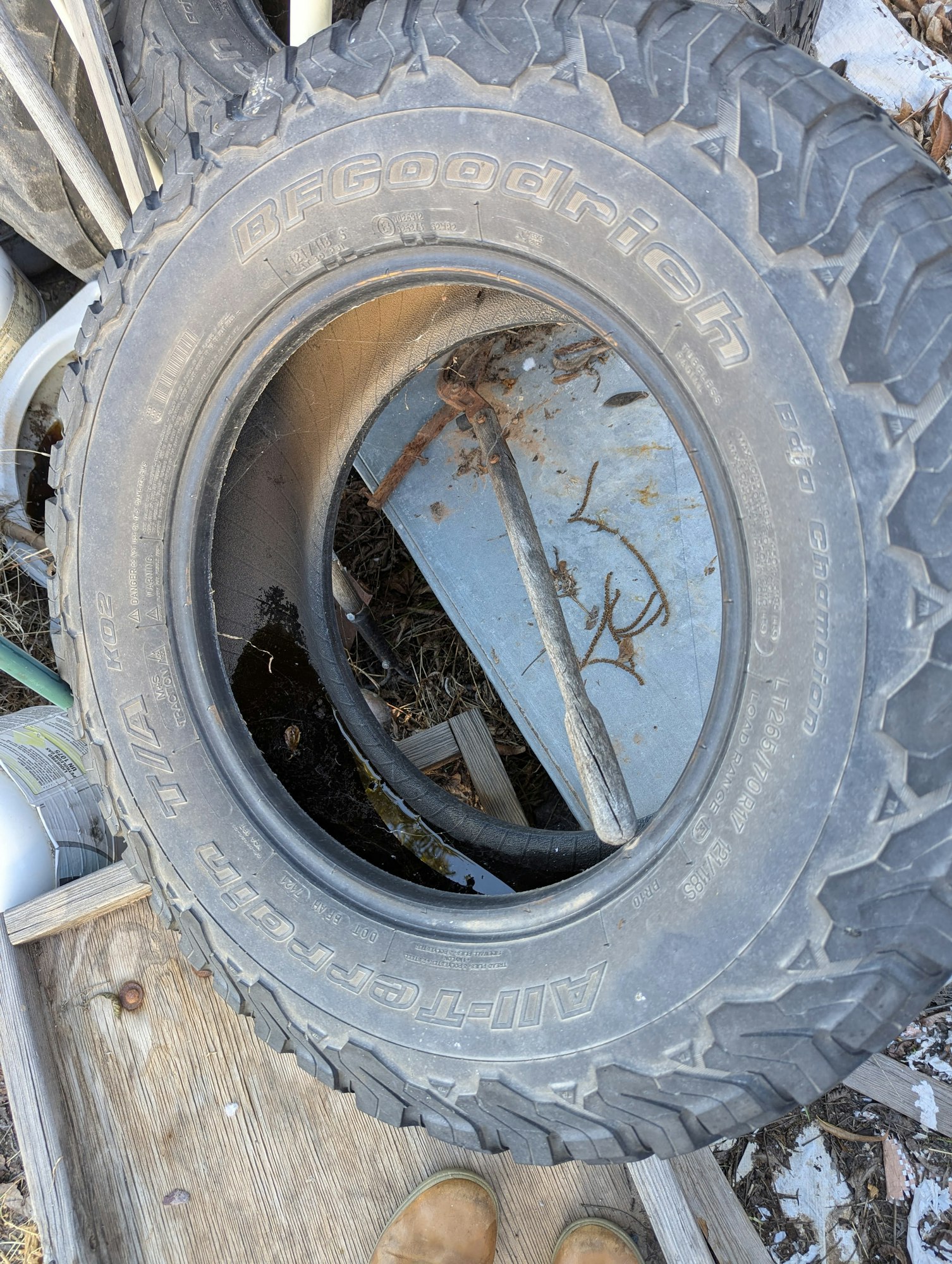 The image shows a tire, labeled "BFGoodrich," resting on a wooden surface with other tires and debris around it.