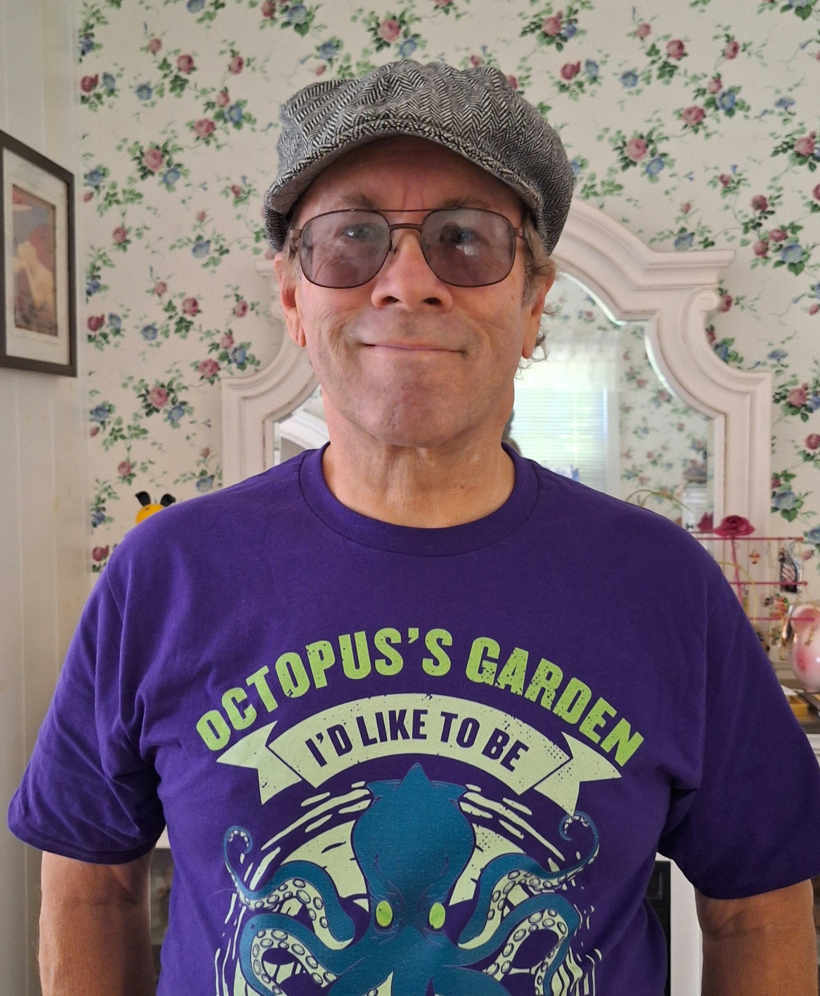 A man in a cap and octopus-themed shirt smiling indoors.