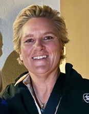 A person with short hair smiling, wearing a black jacket with a logo.