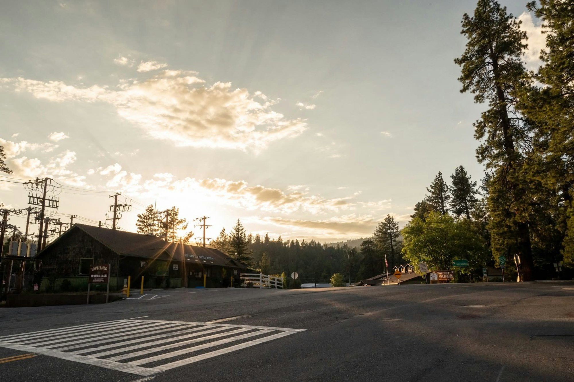 Sunset over a town with trees, utility poles, buildings, and crosswalk on an empty street.