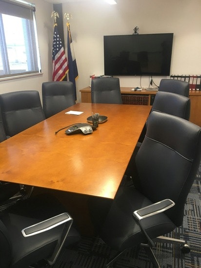 Conference room with a table, chairs, TV, flags, and a phone for calls.
