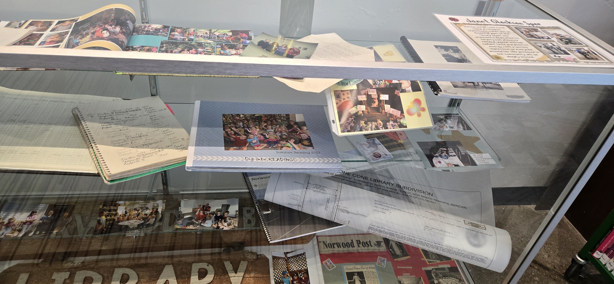 Display case with photo albums, notebooks, and documents related to library and community events.