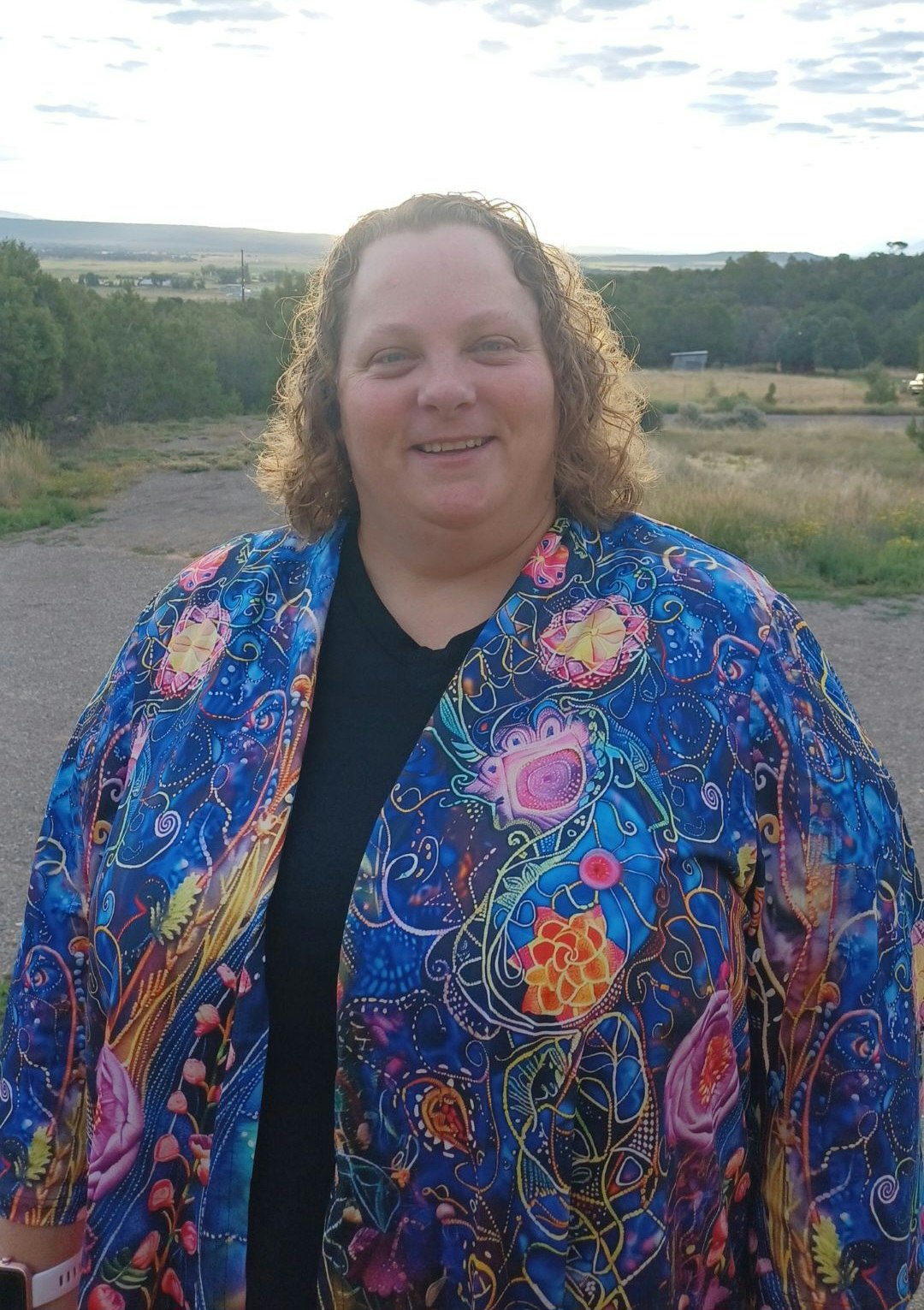 A smiling person wearing a colorful jacket with landscape background.