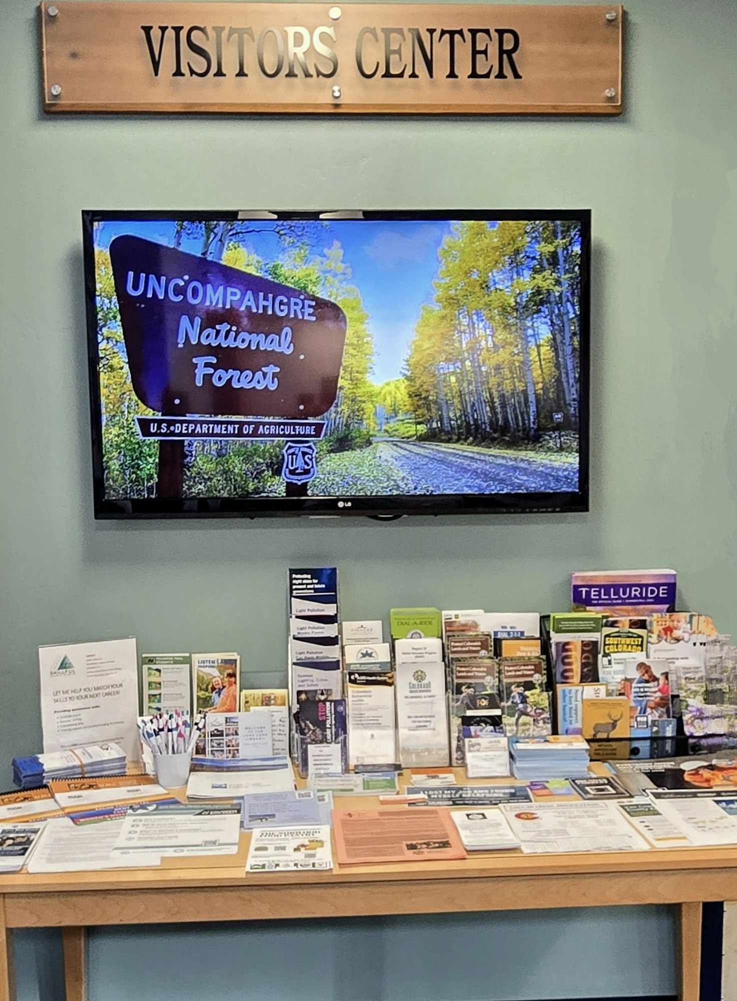 Visitor center display with a TV showing Uncompahgre National Forest and brochures for local attractions.