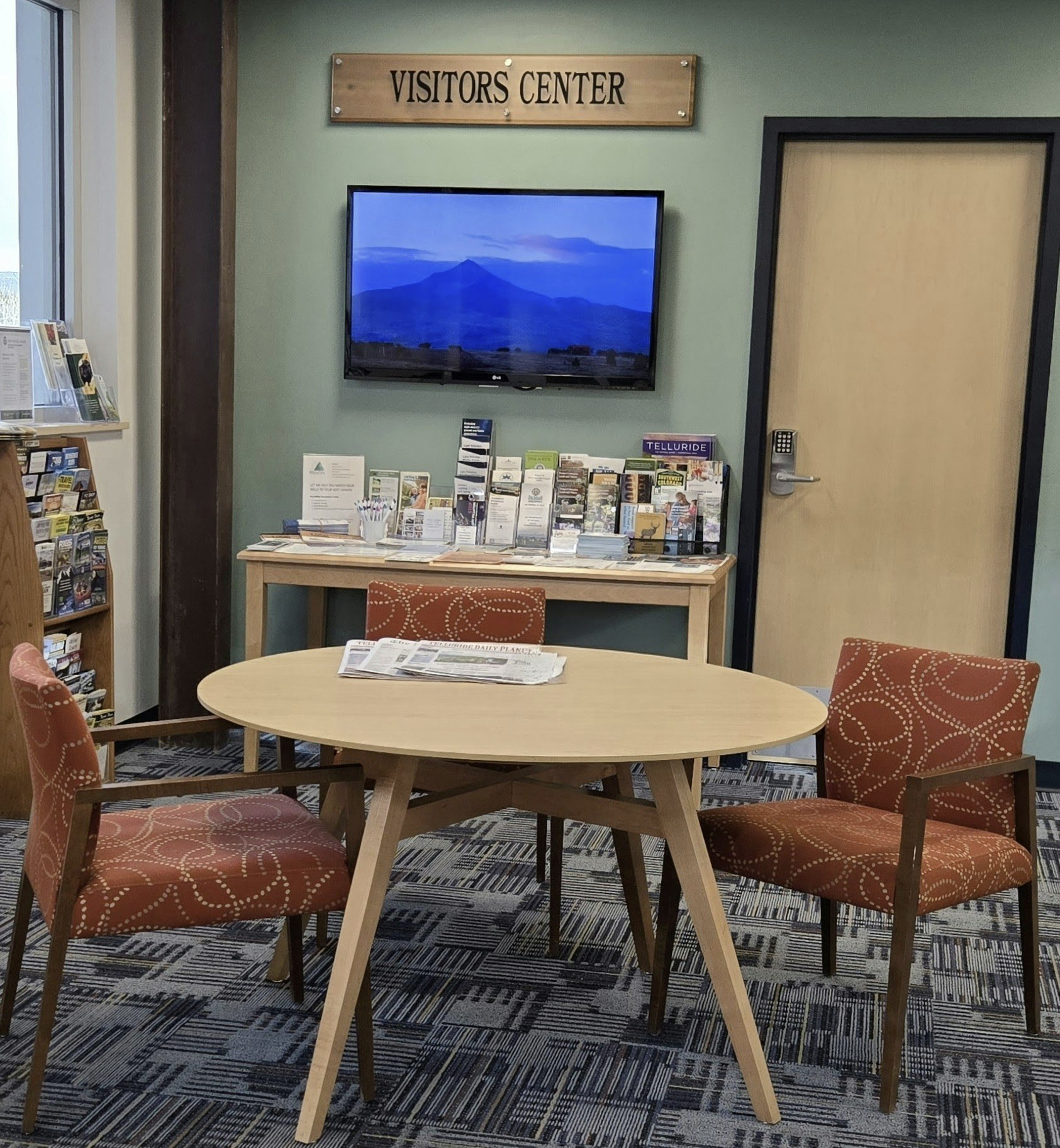 Visitor’s center with a table, chairs, brochures, and a TV displaying a mountain image.