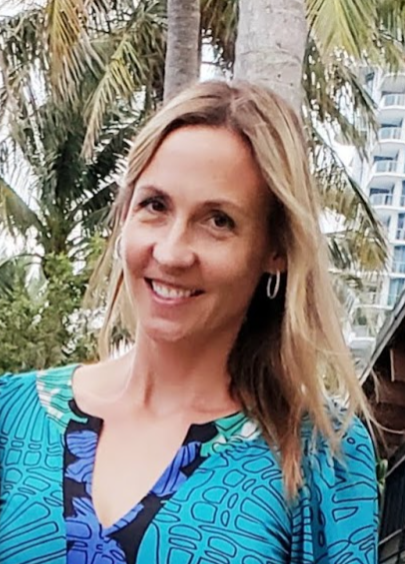 A person smiling outdoors with trees and a building in the background.