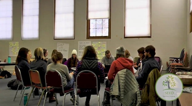 A group of people sitting in a circle in a meeting room with charts and notes on the wall.