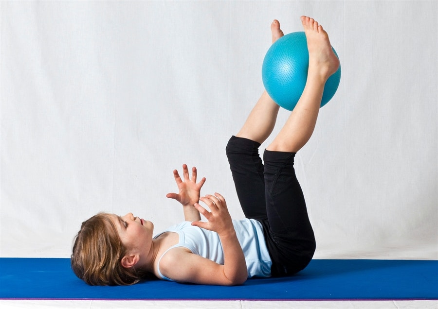 Child balancing a blue ball with feet while lying on a mat.