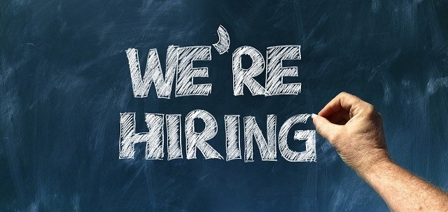 Chalkboard with "WE'RE HIRING" written on it and a hand holding chalk.