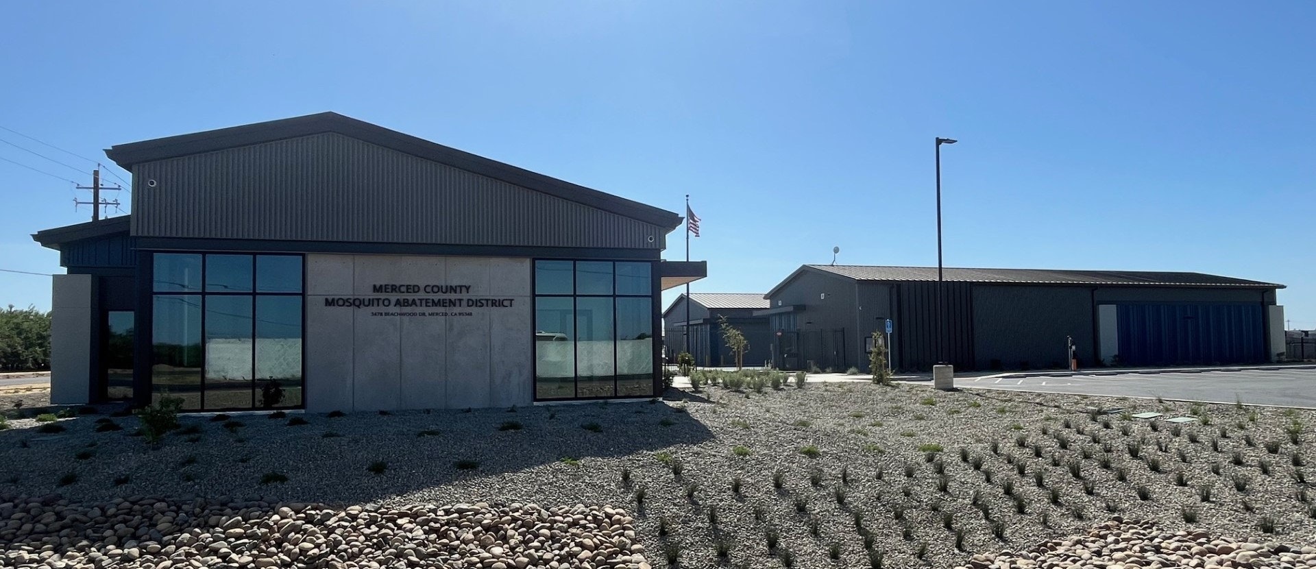 Modern building labeled "Merced County Mosquito Abatement District" with landscaped gravel and plants nearby.