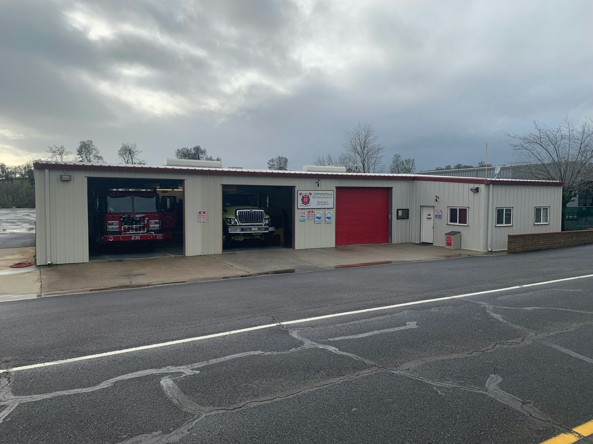 A fire station with two fire engines visible, one red and one yellow, under a cloudy sky.