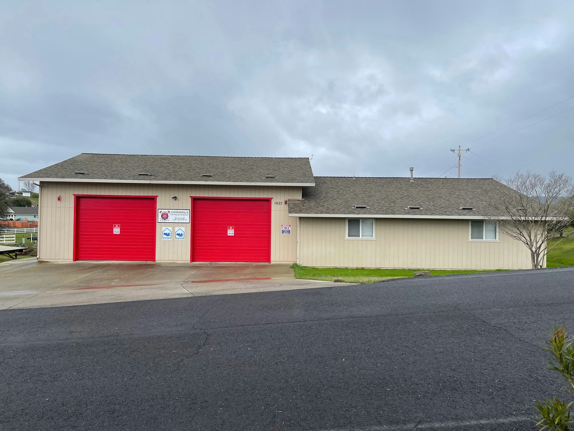 A beige building with two red garage doors, likely a fire station, under a cloudy sky.