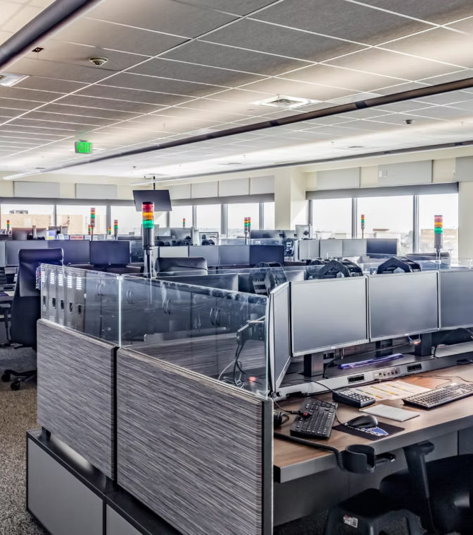 Open-plan office with multiple workstations, monitors, and office chairs. LED signal lights on desks.