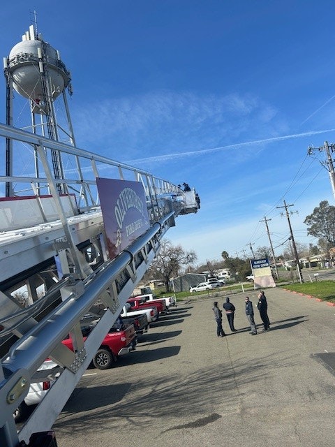 Sideways image of a fire truck ladder extended towards the sky, clear day, people on the ground.