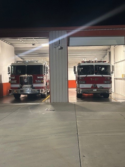 Two fire trucks parked inside a fire station, image is rotated 90 degrees to the left.