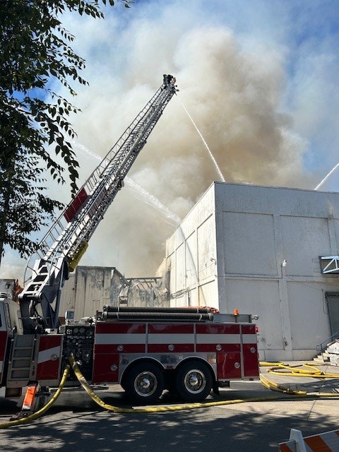 A fire truck with extended ladder spraying water on a smoking building.