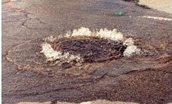 A burst water pipe is causing water to splash out from a circular opening in the road.