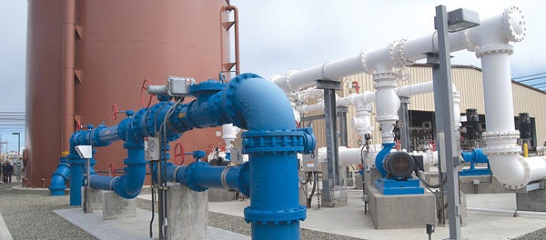 An industrial setup featuring large pipes, valves, and a storage tank, likely part of a water or fluid management system.