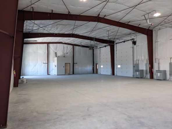 Empty warehouse interior with metal beams, white insulated walls, and concrete flooring.