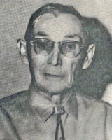 An older man with glasses and a necktie looks at the camera in a black-and-white photo.