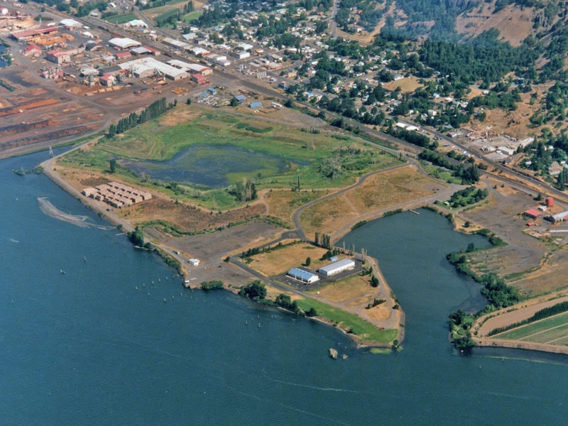 Aerial view of a coastal town with industrial buildings, green fields, and bodies of water.