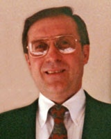A person wearing glasses and a suit with a patterned tie, smiling at the camera.