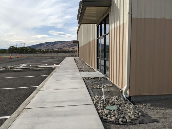 A beige and cream building with large windows, adjacent walkway, empty parking lot, and a scenic mountain backdrop.