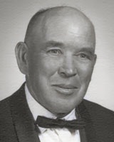 A man in formal attire with a bow tie, posed for a portrait. Black and white photo.