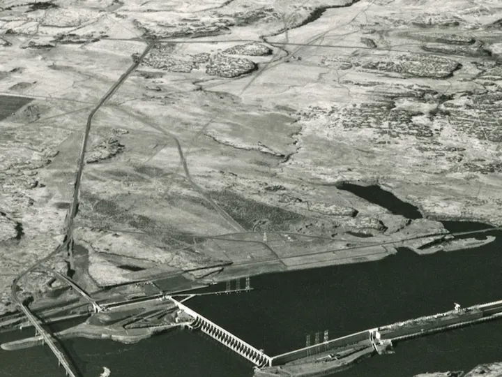 Dam structure with a river and surrounding barren landscape.