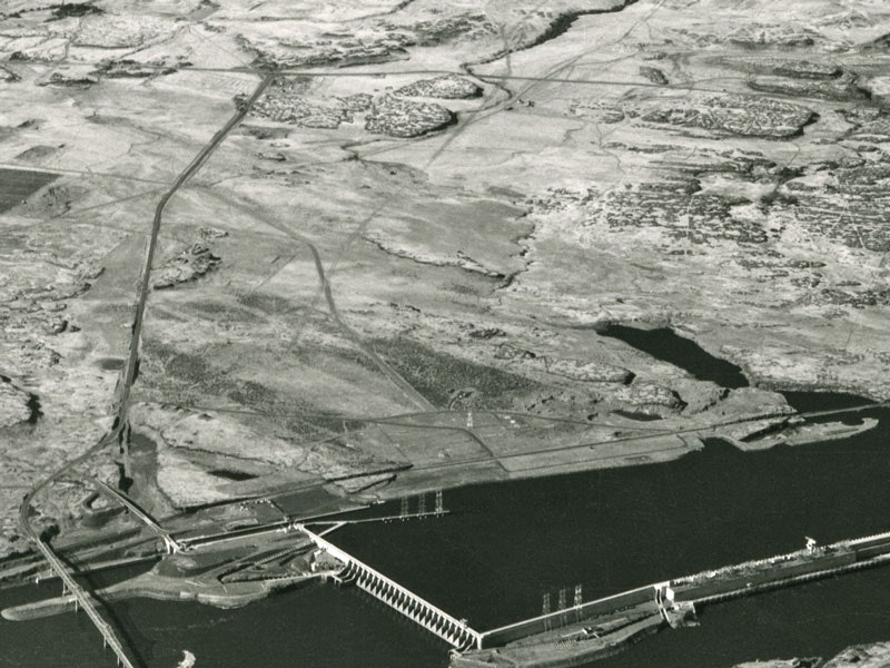 Dam structure with a river and surrounding barren landscape.