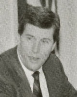 A black and white photo of a man in a suit and tie, seated, looking to the side.