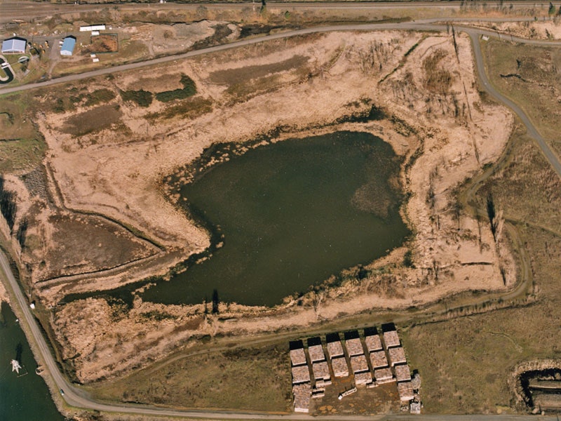 Aerial view of a pond surrounded by vegetation and dirt roads, with several rectangular structures in the foreground.