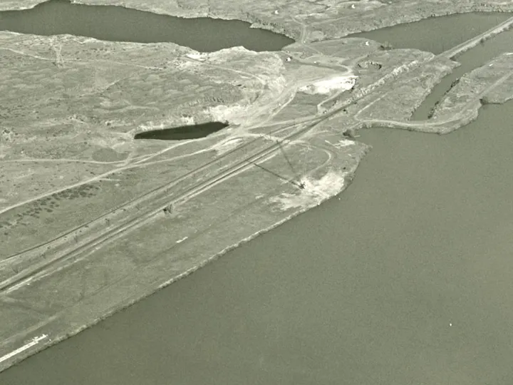 Aerial view of a river with surrounding land, roads, and a bridge crossing over. Sparse vegetation and infrastructure visible.