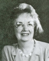 A black and white portrait of a smiling person with glasses and curly hair, wearing a blazer and necklace.