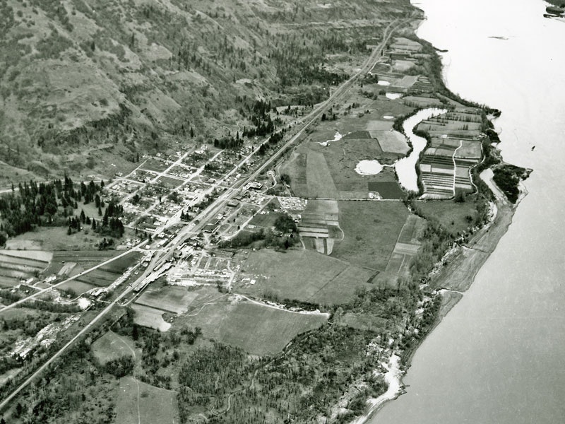 Aerial view of a rural landscape with fields, a river, and a small town, surrounded by hills and scattered trees.