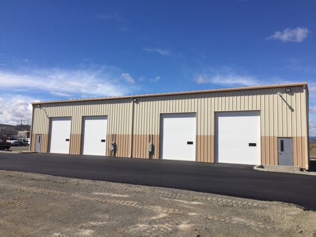 A beige metal building with four large garage doors under a clear blue sky.