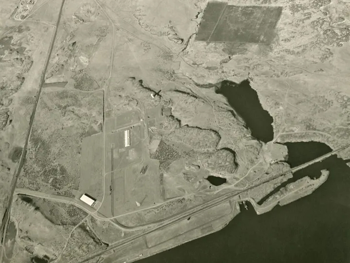 Aerial view of a landscape with roads, a runway, buildings, and a body of water.