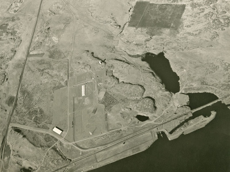 Aerial view of a landscape with roads, a runway, buildings, and a body of water.