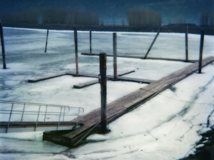 A wooden dock partially submerged in ice on a frozen lake, with posts and a viewing platform.