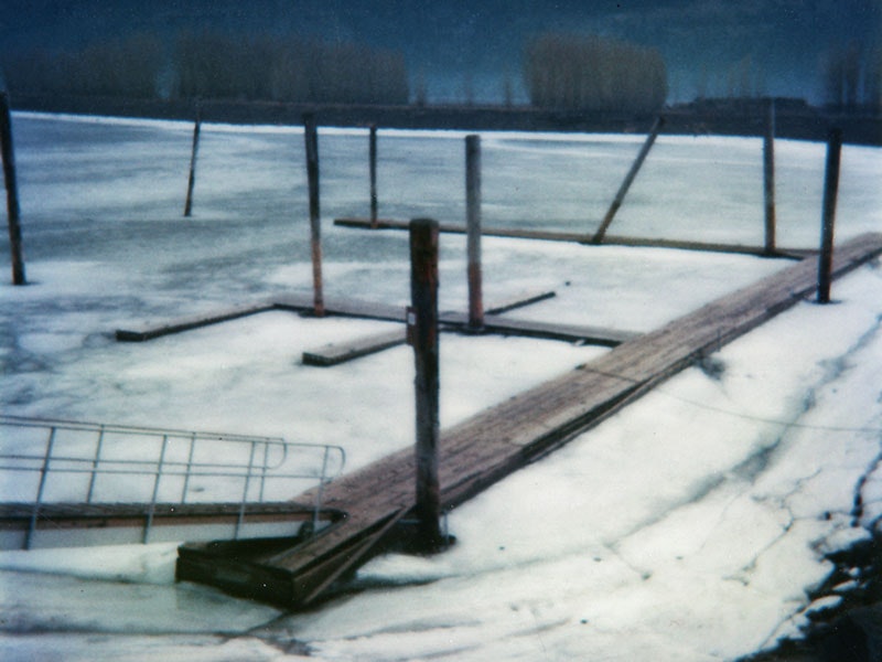 A wooden dock partially submerged in ice on a frozen lake, with posts and a viewing platform.