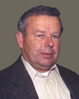 A person wearing a suit jacket and shirt is shown against a plain background.