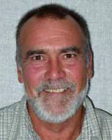Image of a man with a beard, wearing a checkered shirt, smiling at the camera.