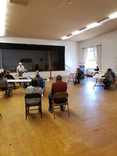 People seated in a hall with one person standing at the front, possibly in a meeting or class.